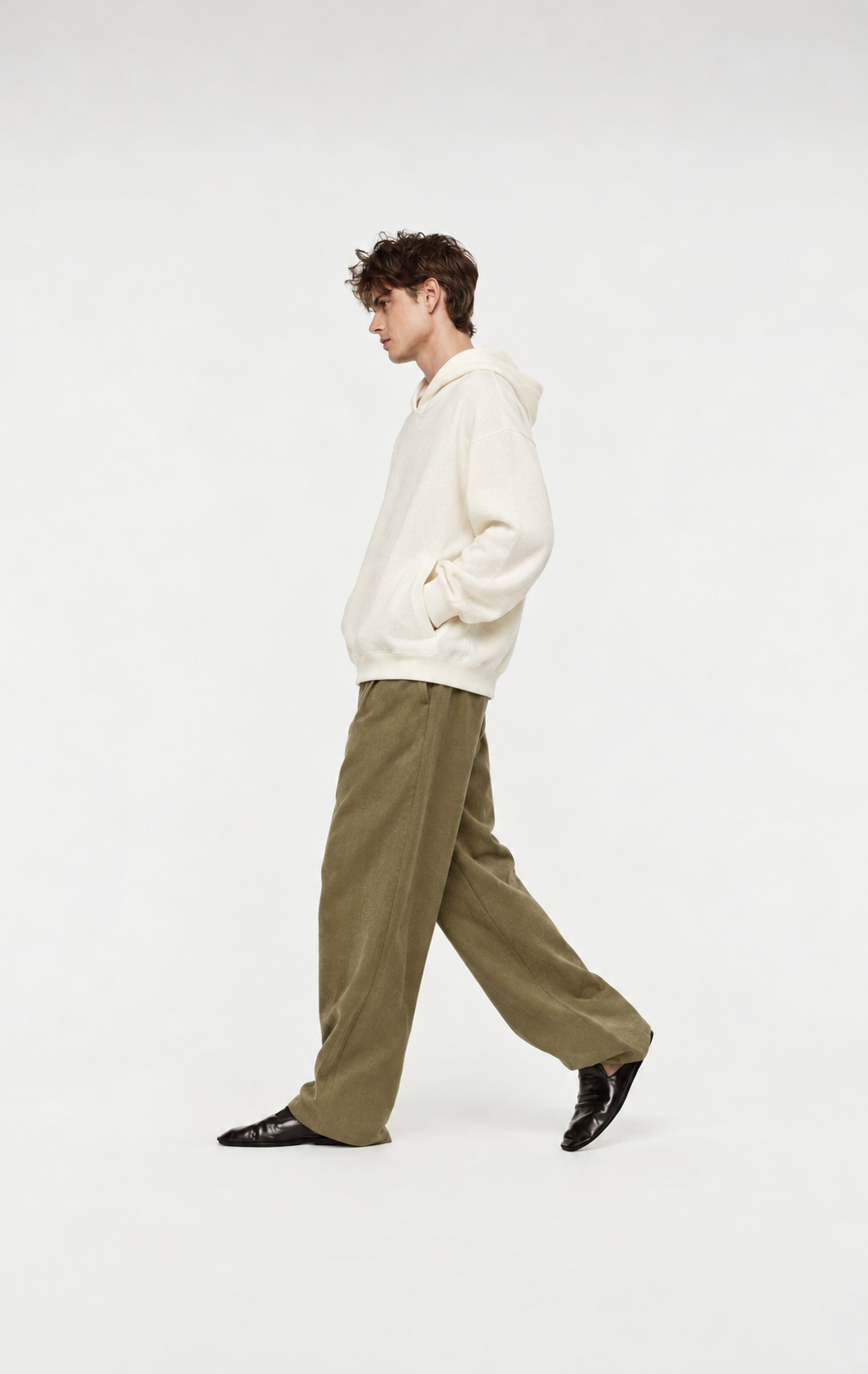 A model walking in profile wearing an ivory hoodie and olive trousers