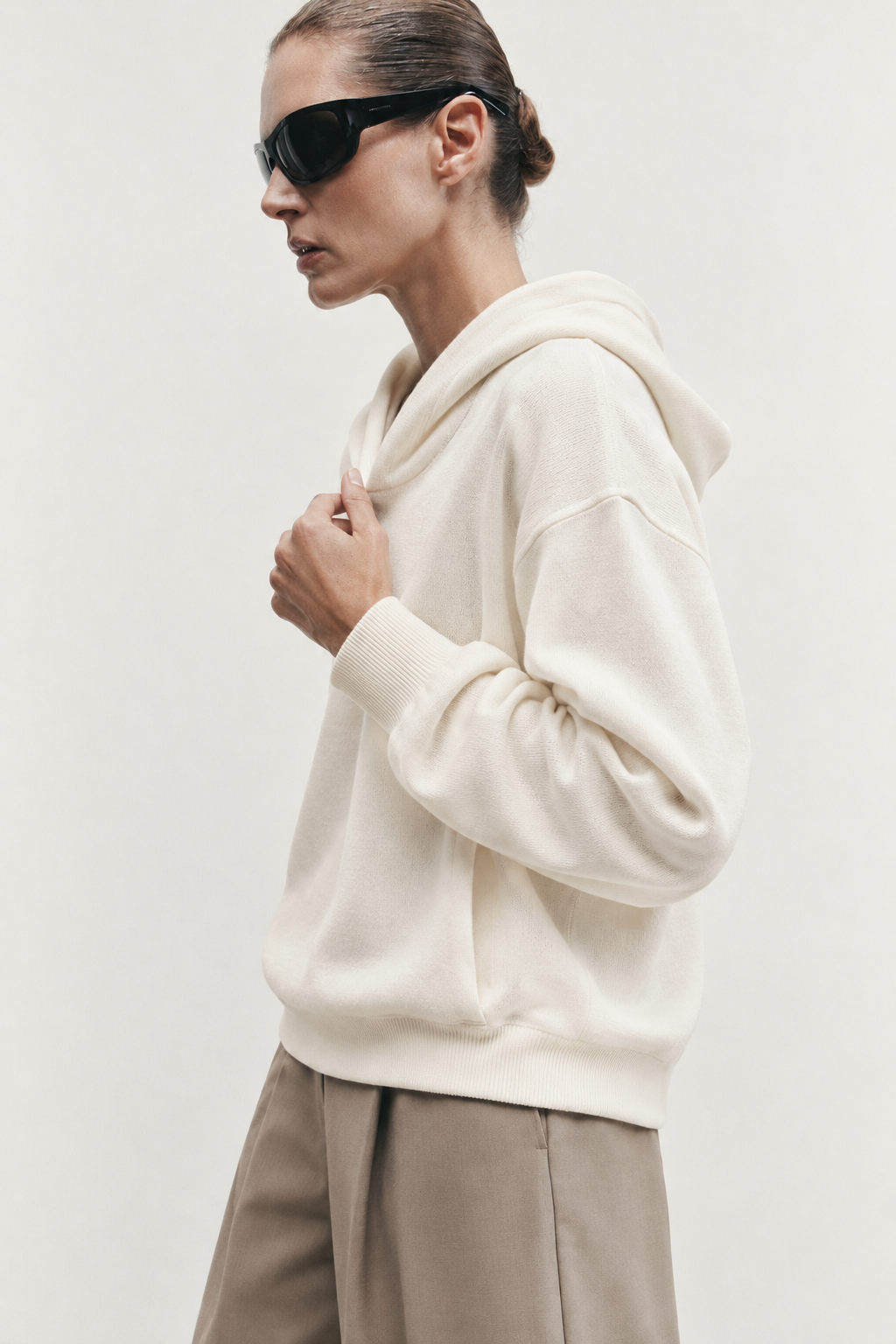 Side-profile portrait of a woman wearing an ivory knit hoodie and sunglasses
