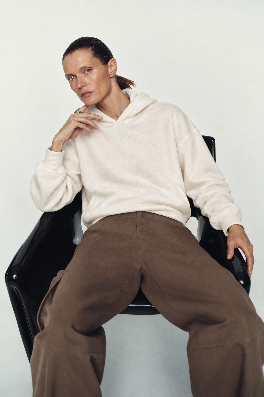 A seated woman wearing an ivory knit hoodie and brown trousers